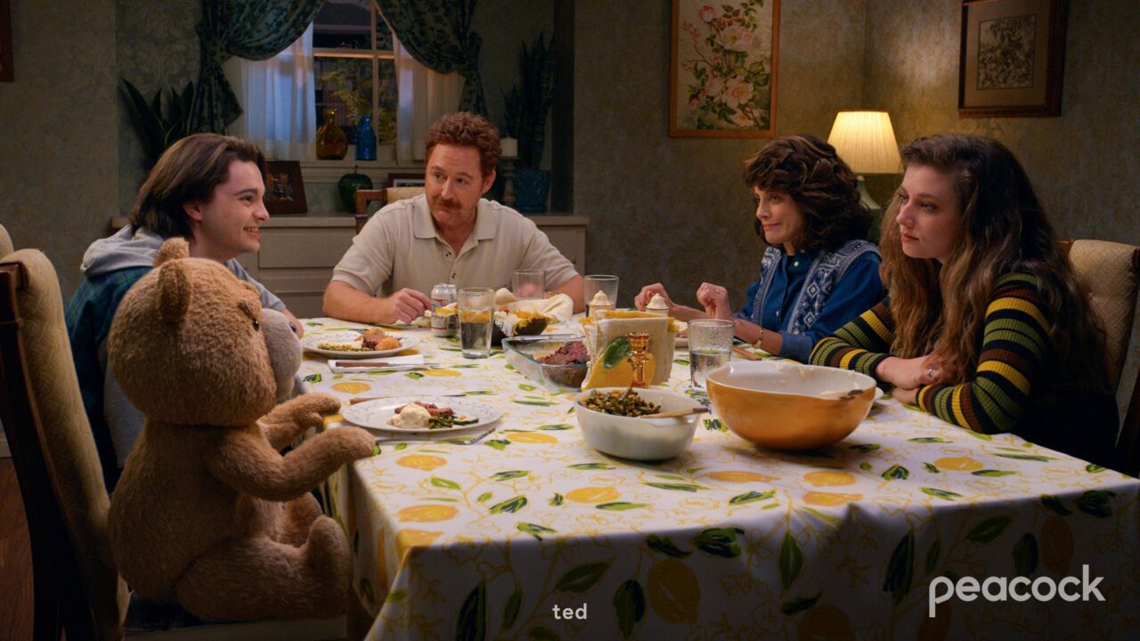Kadr z serialu "Ted". Rodzina siedzi przy stole wraz z tytułowym bohaterem - pluszowym misiem.