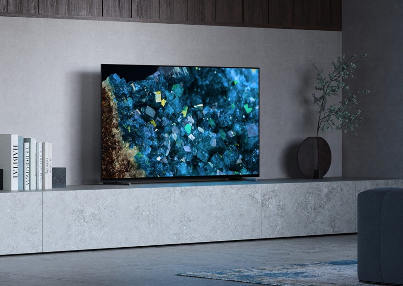 Telewizor Sony Bravia OLED A80L ustawiony na kamiennej półce. Po lewej stronie widać ksiażki, a po prawej wazonmateriały prasowe