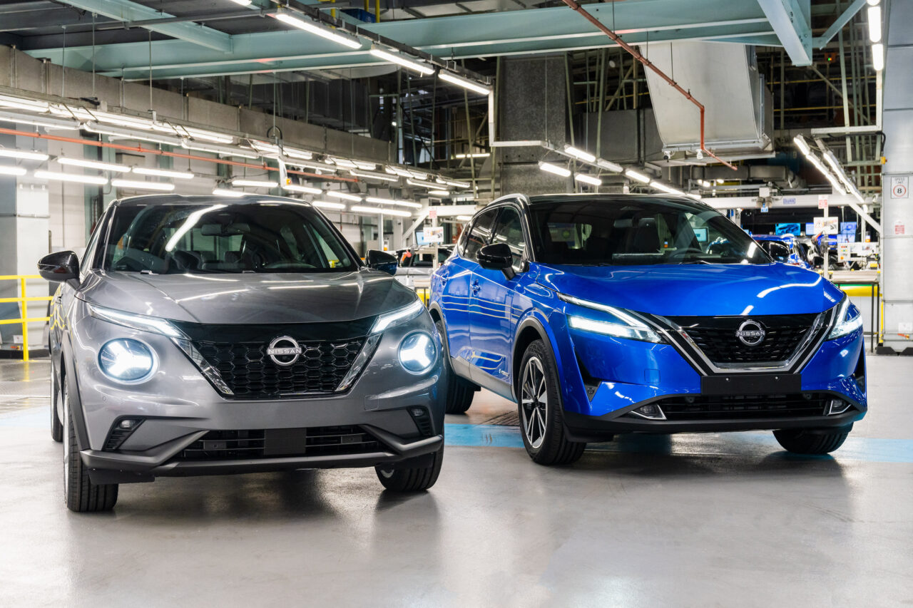 Dwa samochody elektryczne marki Nissan. Jeden szary, drugi niebieski, stoją w fabryce japońskiej firmy gotowe do jazdy.

