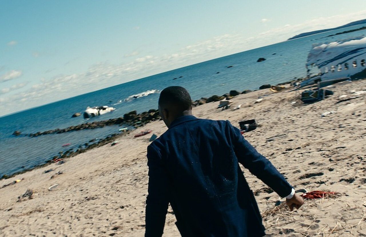Kadr z filmu Zostaw świat za sobą od Netflix przedstawiający mężczyznę na plaży wśród śmieci i fragmentów rozbitego samolotu
