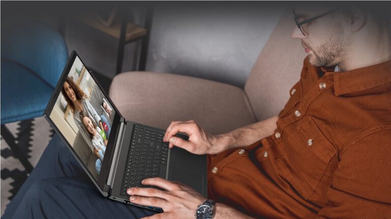 Mężczyzna w pomarańczowej koszuli siedzący na kanapie używa laptopa do wideorozmowy z dwiema osobami.