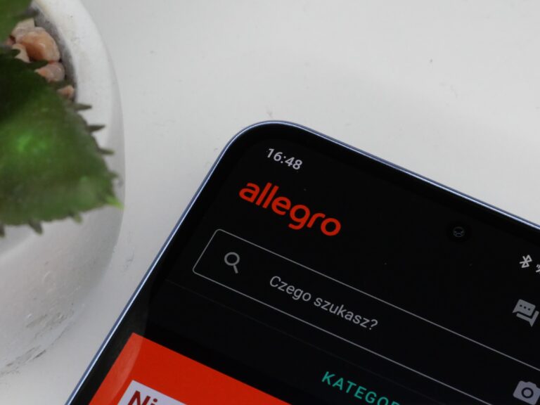 Smartfon z włączoną aplikacją Allegro. Urządzenie leży na białym tle