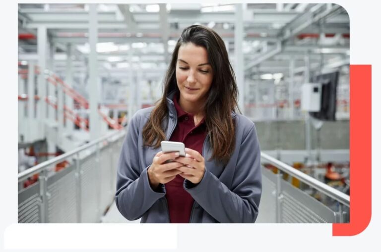 Kobieta w biznesowym ubiorze korzysta z telefonu komórkowego na korytarzu przemysłowej hali produkcyjnej.