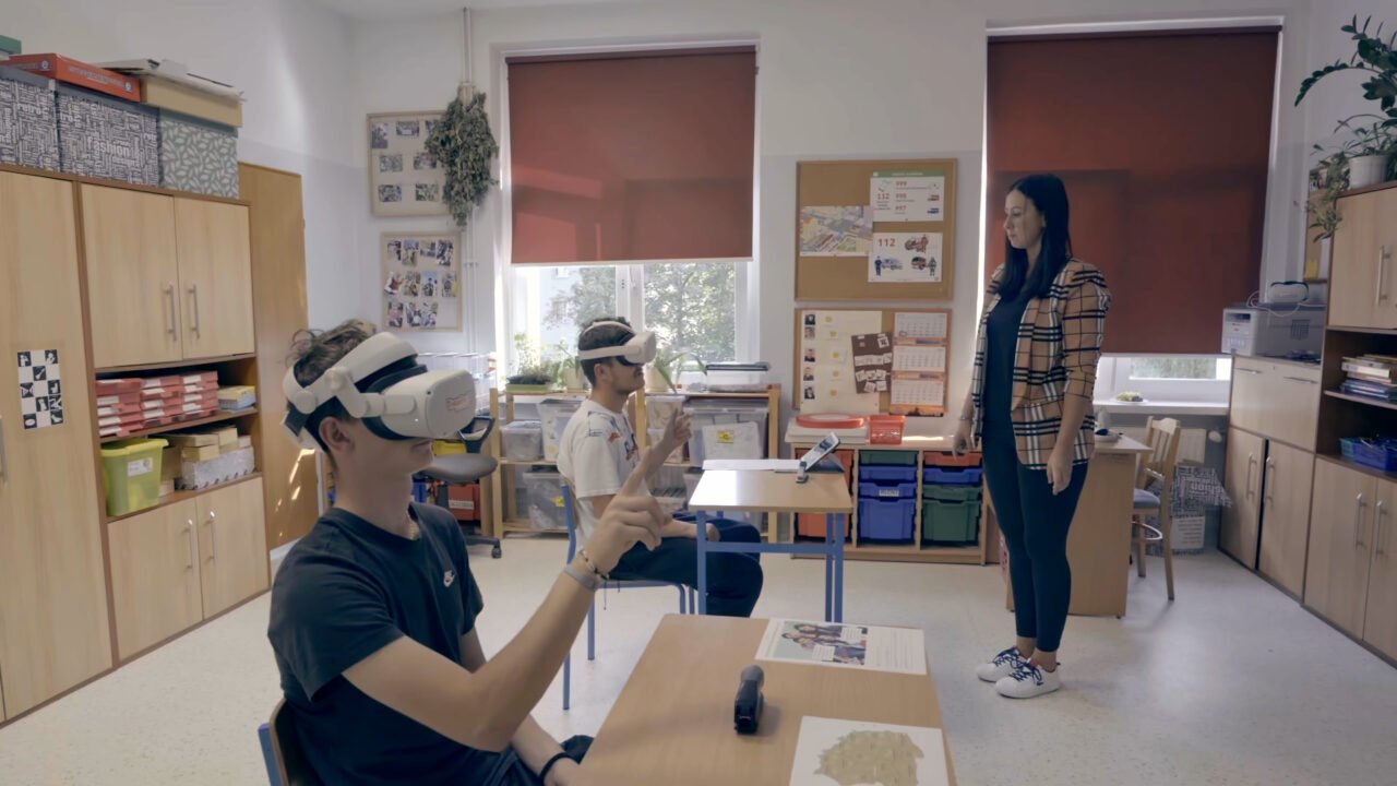 szkolna sala, a w niej dwóch młodych chłopaków w goglach VR na głowie. Przed nimi stoi terapeutka