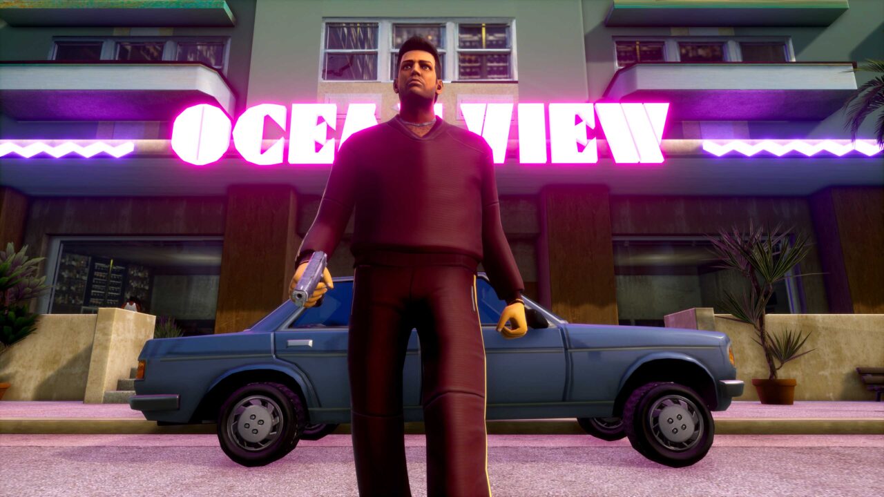 Postać z gry wideo GTA ubrana w bordowy kombinezon stoi przed budynkiem z neoneowym napisem "OCEANVIEW" i samochodem w tle. Gra niebawem trafi na Netflix 