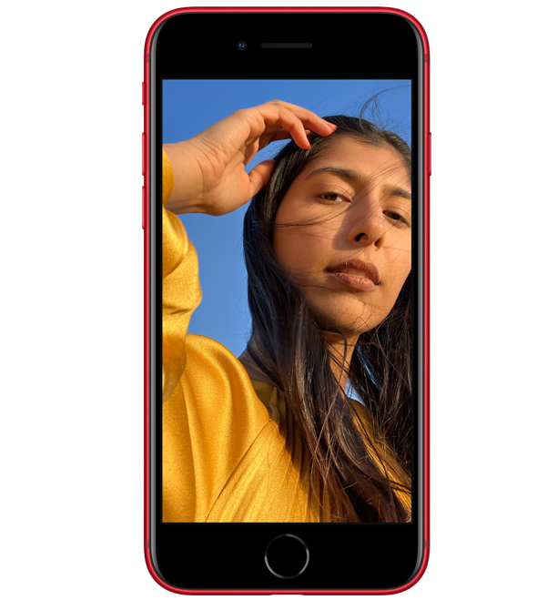 Młoda kobieta w żółtym ubraniu pozująca na selfie na ekranie czerwonego smartfona, na tle niebieskiego nieba.