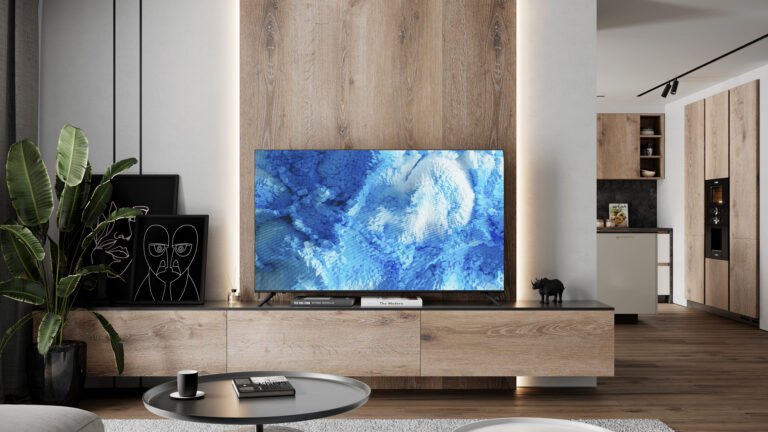 Telewizor KIVI postawiony na drewnianej szafie RTV na tle podświetlanej ściany