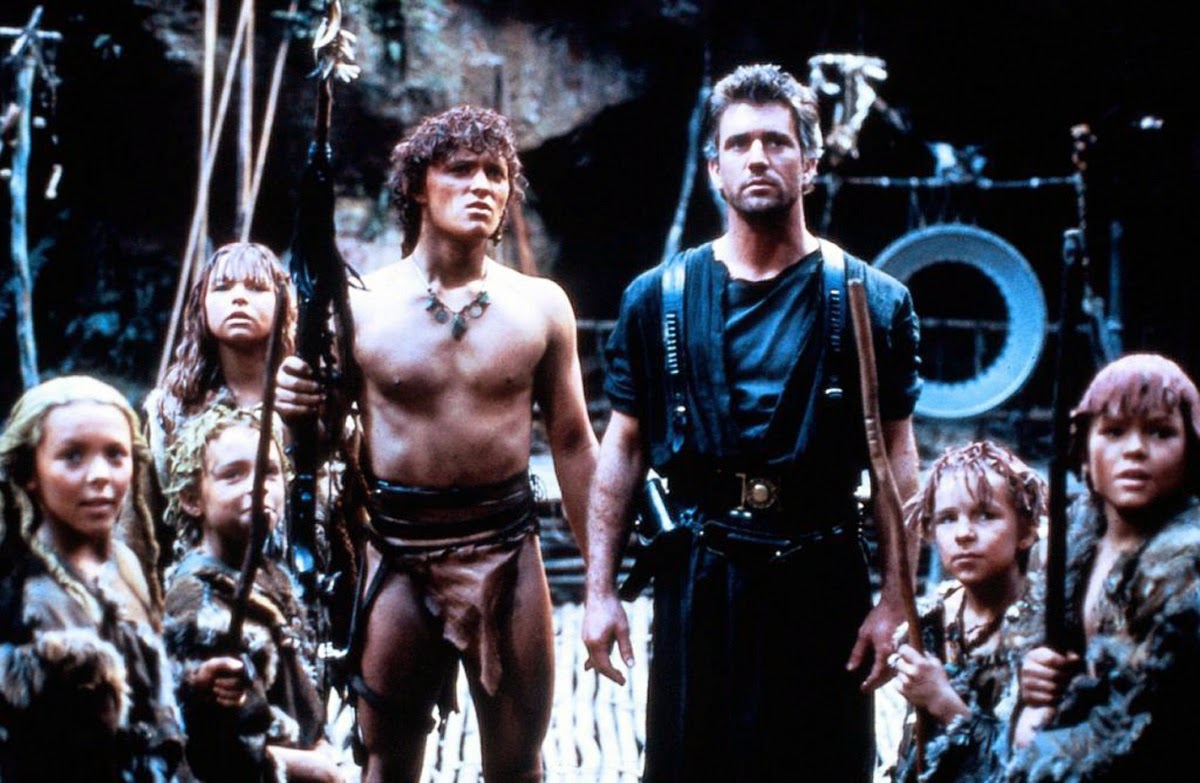 Grupa postaci z filmu fantasy, w tym dwóch mężczyzn dorosłych i kilkoro dzieci w dzikich strojach, stojących razem z wyrazami powagi na twarzach.