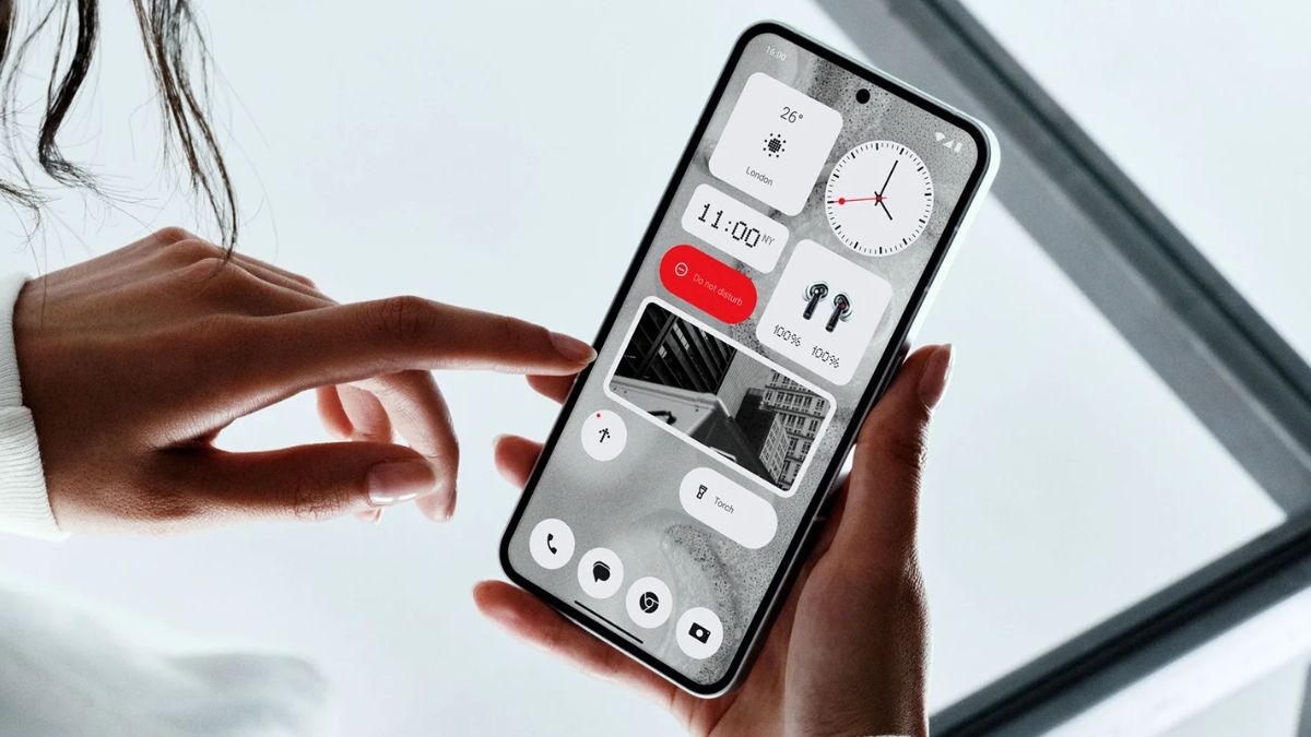 Osoba trzymająca smartfon z otwartą aplikacją do zarządzania inteligentnym domem, pokazującą kontrolki takie jak zegar, temperatura i opcje oświetlenia.
