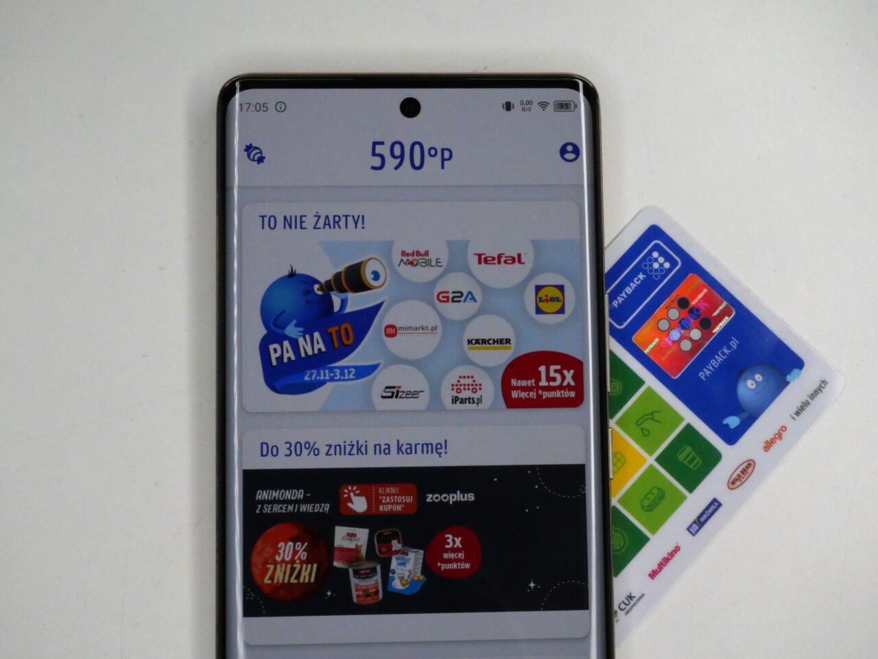 Smartfon wyświetlający ekran aplikacji z ofertami i punktami lojalnościowymi, leżący obok karty lojalnościowych.