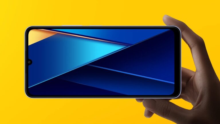 Smartfon trzymany w dłoni na żółtym tle, wyświetlacz prezentuje grafikę z niebieskimi i jasnoniebieskimi trójkątami na ciemnym tle.