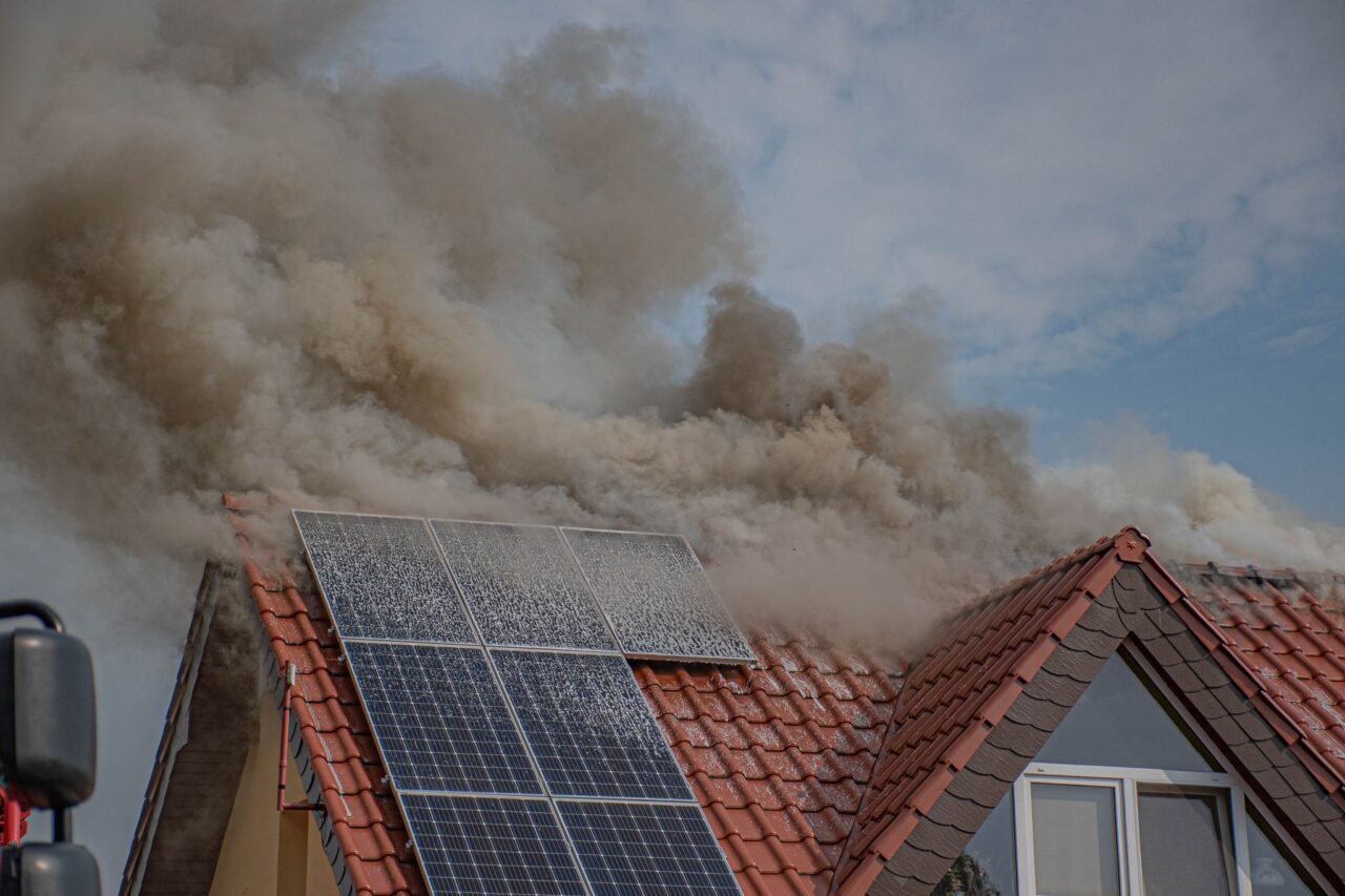 Dach domu z panelami słonecznymi, z którego wydobywa się gęsty, szary dym. pożary fotowoltaiki w polsce, dom mieszkalny 