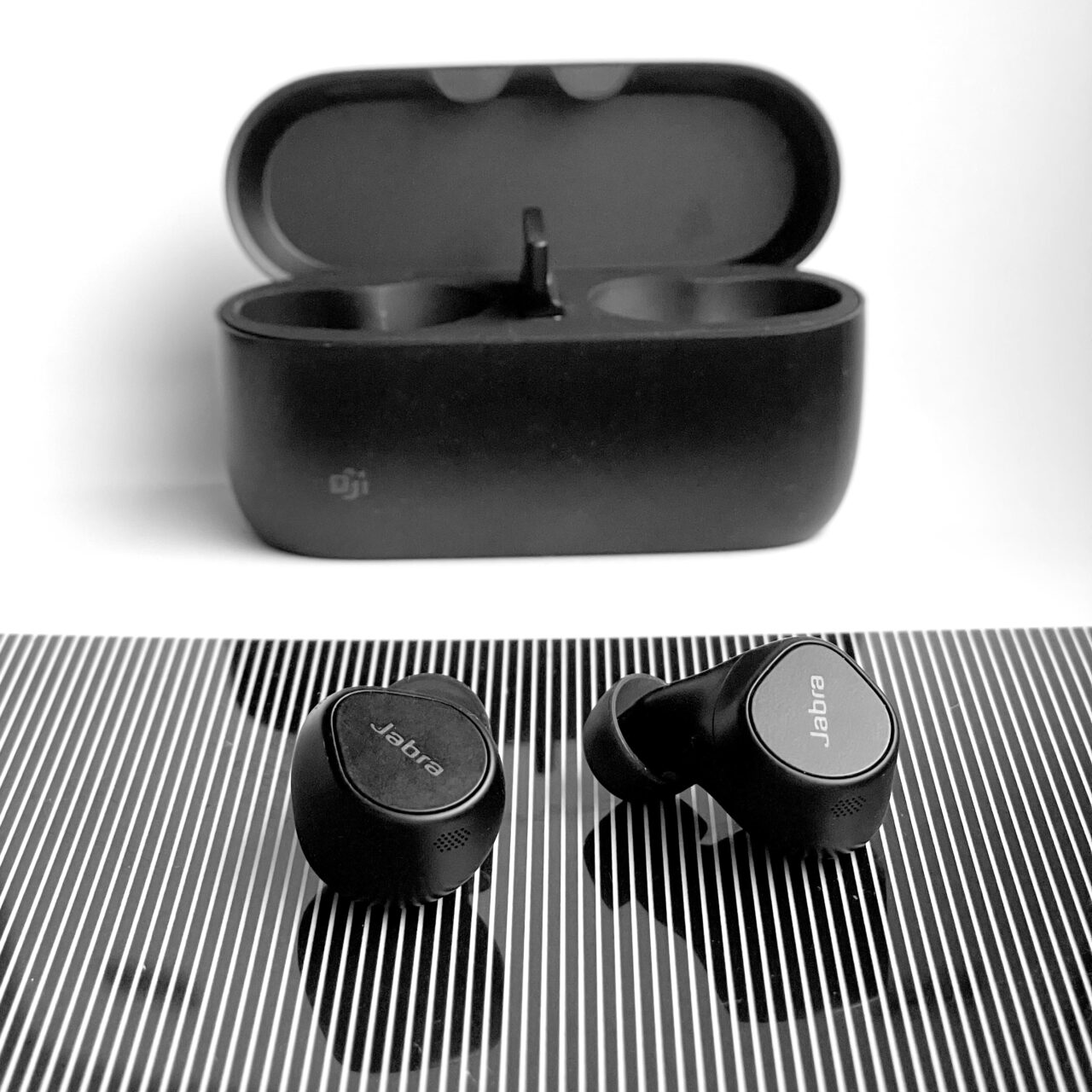 Czarno-białe zdjęcie bezprzewodowych słuchawek dousznych marki Jabra Evolve2 Buds i ich etui ładującego.