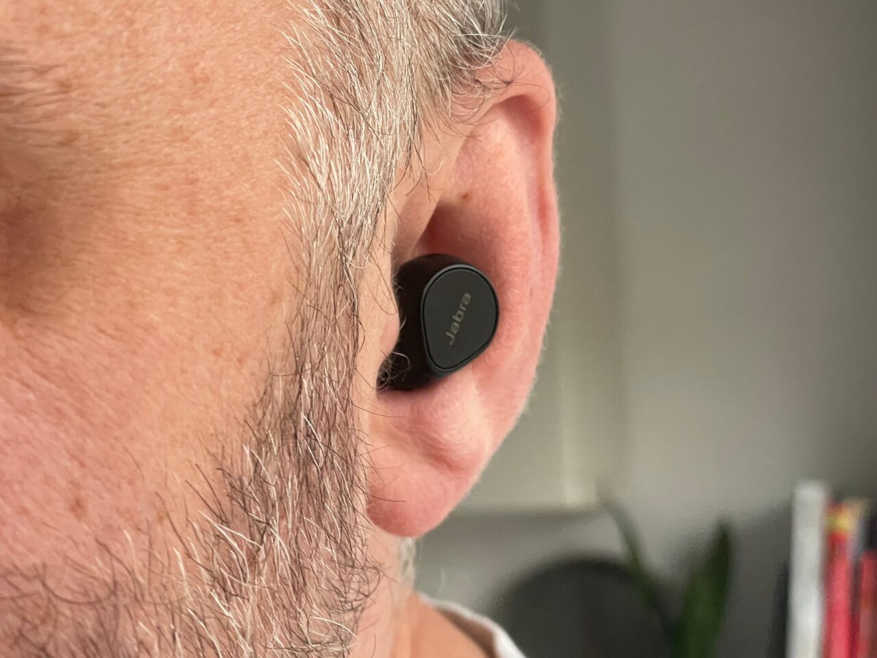 Częściowy widok mężczyzny z siwym zarostem na twarzy i słuchawką w uchu.