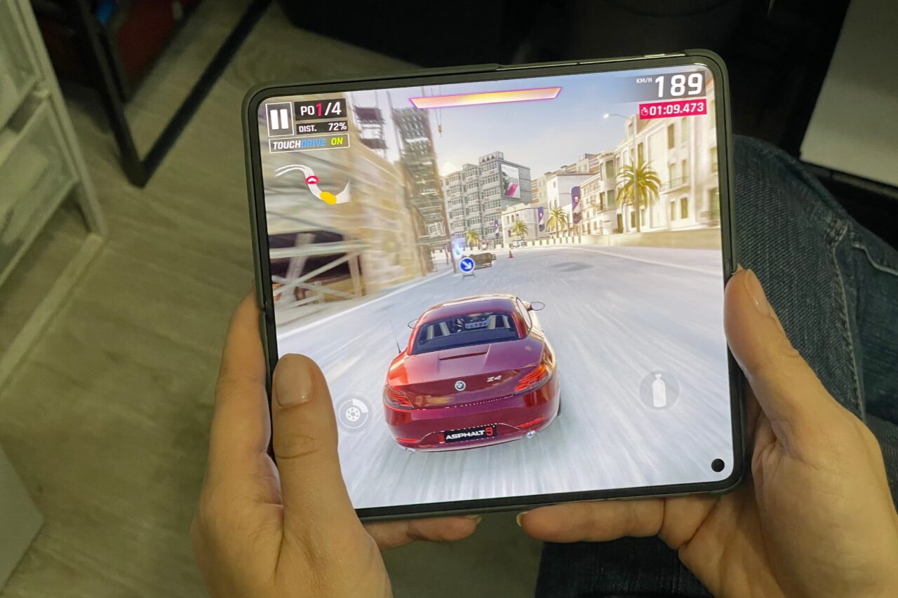 Osoba trzymająca smartfon z wyświetlaną grą wyścigową, na ekranie czerwony samochód wyścigowy w miejskim otoczeniu. recenzja oneplus open