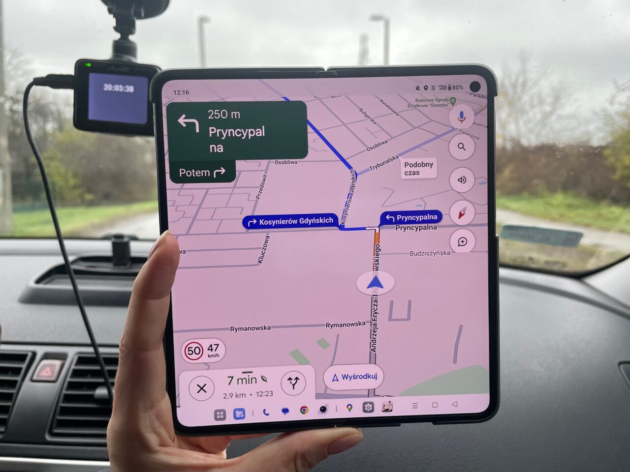 Osoba trzymająca telefon z włączoną aplikacją nawigacyjną wewnątrz samochodu. Na tablet pokazano mapę z trasą i wskazówkami dojazdu. recenzja oneplus open