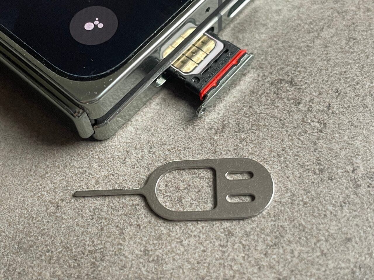 Klucz SIM leżący na szarym blacie obok częściowo otwartej szufladki na kartę SIM w smartfonie. recenzja oneplus open