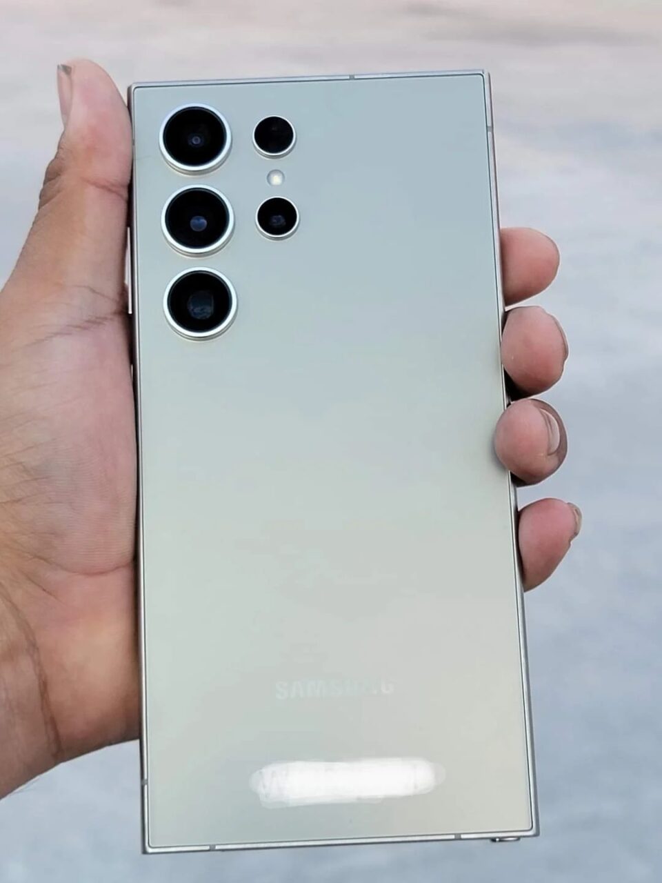 Tylna strona smartfona Samsung Galaxy S24 w kolorze białym trzymana w dłoni, z pięcioma obiektywami aparatu i logo producenta.