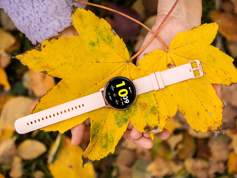 Ręka trzymająca żółty liść, na którym spoczywa inteligentny zegarek z białym paskiem