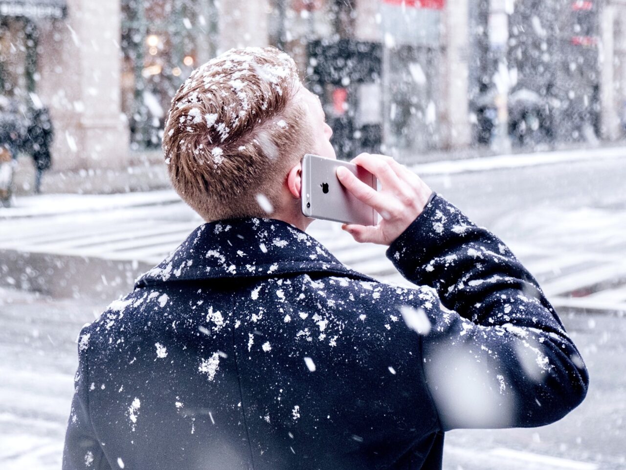 telefon Apple iPhone trzymany przez mężczyznę, którego mogło spotkać oszustwo na telefon z banku, prowadzi on rozmowę telefoniczną na dworze, pada śnieg
