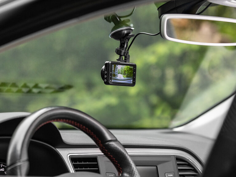 Widok z wnętrza samochodu na kamerę samochodową zamocowaną na szybie, która wyświetla obraz drogi.