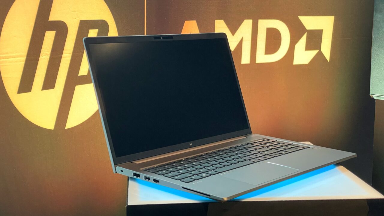 Laptop marki HP na tle z logo HP i AMD na ścianie.