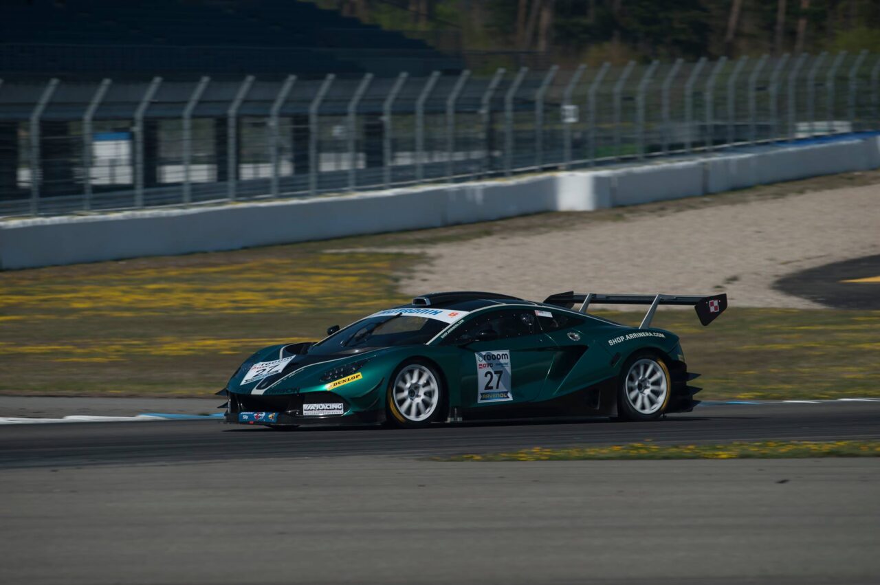 Zielono-czarny samochód wyścigowy Arrinera Hussarya jedzie z dużą prędkością po torze wyścigowym w słoneczny dzień.