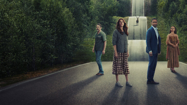 Cztery osoby stoją na asfaltowej drodze, otoczonej przez zielone drzewa, zwrócone w stronę obserwatora. Od lewej: mężczyzna w zielonej koszuli i jeansach, kobieta w szarej kurtce i wzorzystej spódnicy, mężczyzna w ciemnoniebieskim garniturze oraz kobieta w brązowej sukience. W tle na środku drogi widać jelenia.