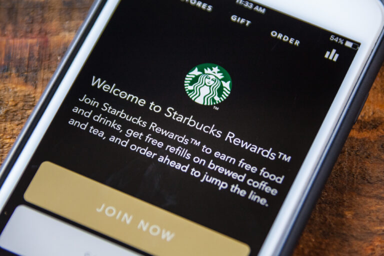 Smartfon wyświetlający ekran aplikacji Starbucks Rewards z tekstem powitalnym i przyciskiem "JOIN NOW".