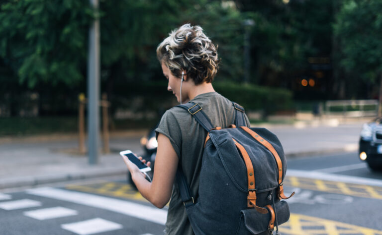 Osoba z plecakiem przeglądająca smartfon przy przejściu dla pieszych. Nowe rozwiązanie od Orange ma sprawić, że takie osoby będą na pasach bezpieczniejsze.