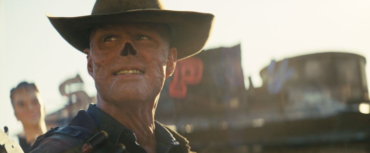 Mężczyzna w kapeluszu kowbojskim na tle rozmytego zachodniego miasteczka.