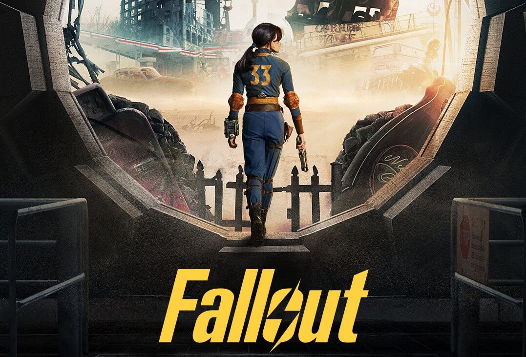Postać w stroju z numerem 33 patrzy na zniszczony, postapokaliptyczny krajobraz z opuszczonymi pojazdami i ruinami budynków, stojąc na progu ze złomem i napisem "Fallout" na pierwszym planie.