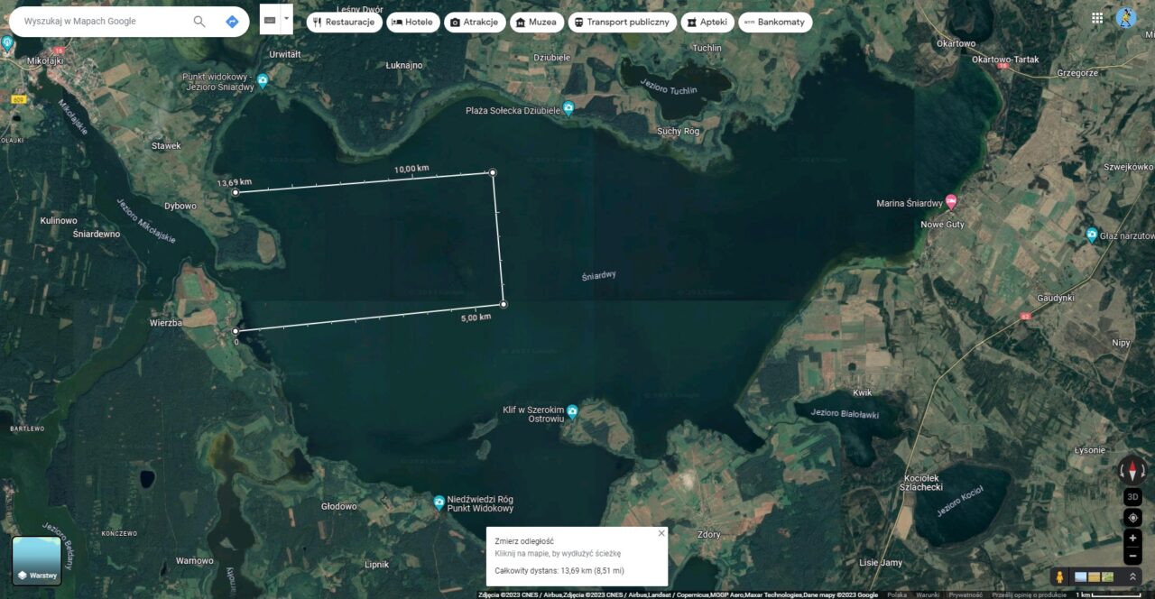 Zrzut ekranu widoku satelitarnego z Map Google pokazujący teren jeziora z naniesionymi liniami pomiarowymi odległości.