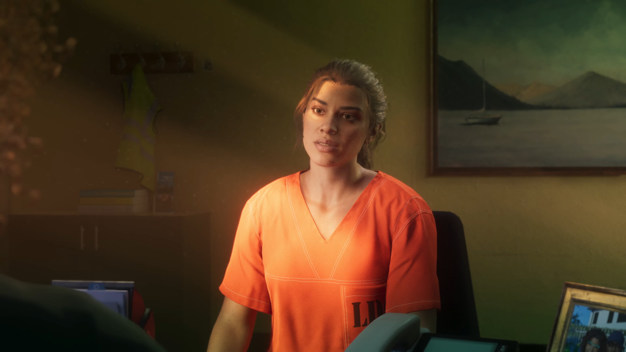 Kobieta w pomarańczowym uniformie więziennym siedzi w pokoju z żółtymi ścianami przy biurku z widocznymi przedmiotami osobistymi i obrazem na ścianie. To screenshot z trailera GTA 6, zapisywanego także jako GTA VI
