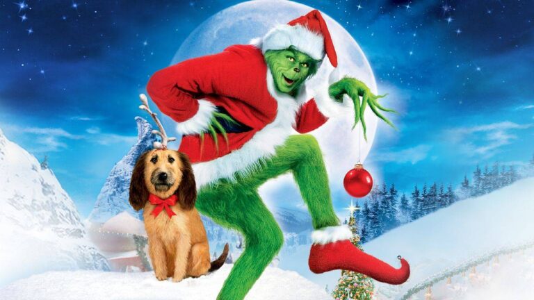 Zielona postać Grincha w czerwonym stroju Świętego Mikołaja, z jedną ręką opartą o biodro, a w drugiej trzymająca czerwoną bombkę. Obok Grincha siedzi pies z czerwoną kokardą i porożem renifera. W tle śnieżny krajobraz, góry, choinki oraz wielki księżyc.