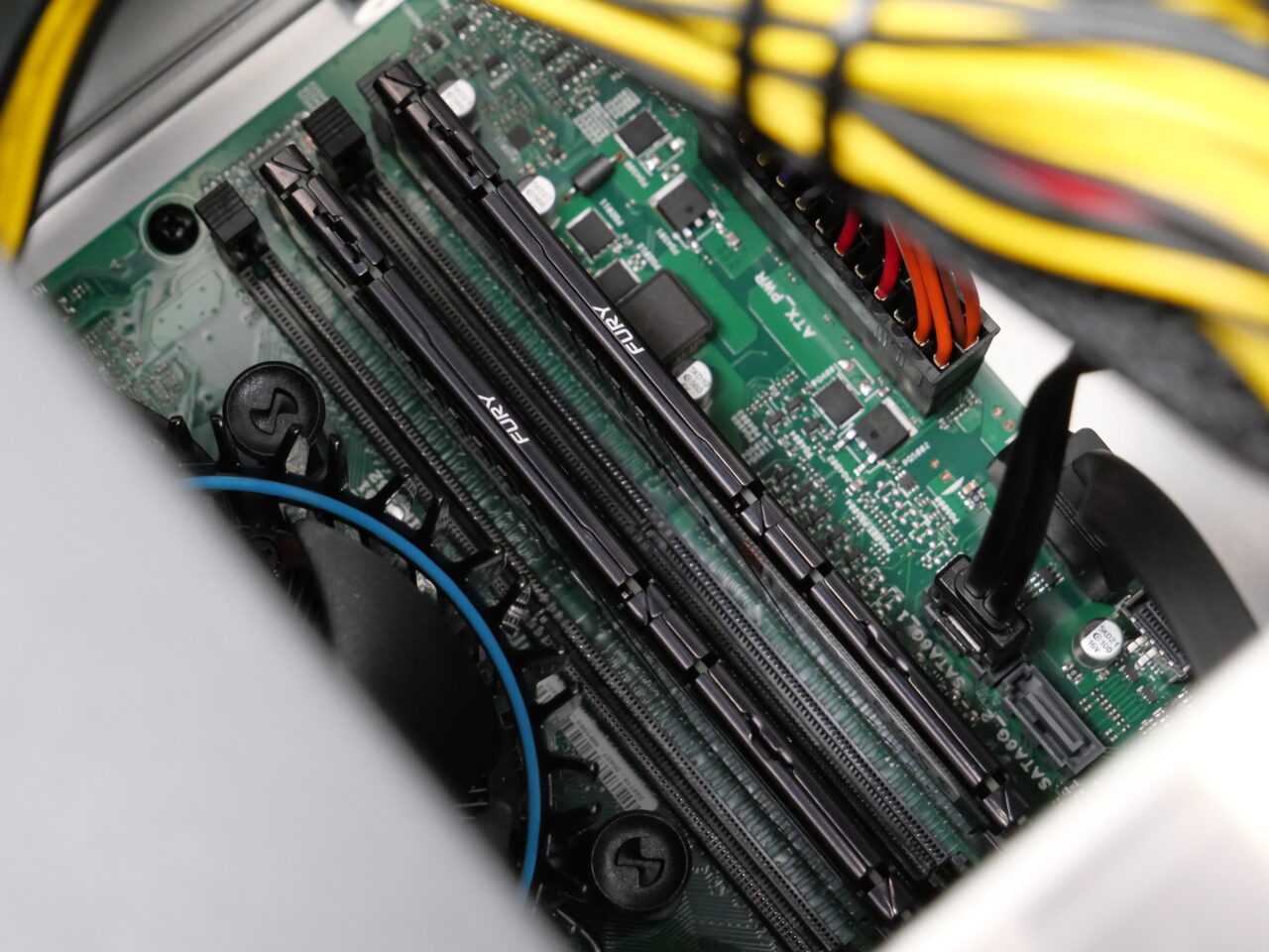 Wnętrze otwartej obudowy komputera z widocznymi slotami na pamięć RAM, kablami i częścią wentylatora chłodzącego.