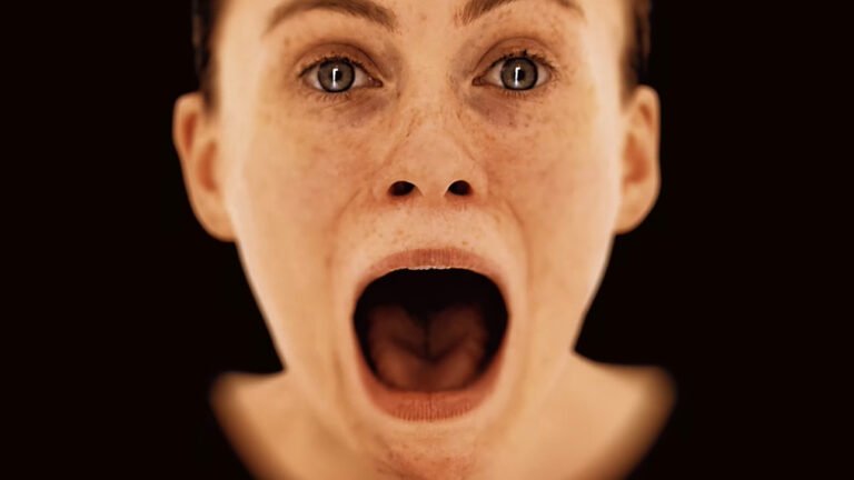 Kobieta z szeroko otwartymi oczami i ustami wyrażającymi zdumienie lub strach, na czarnym tle. Screen z trailera OD od Hideo Kojima
