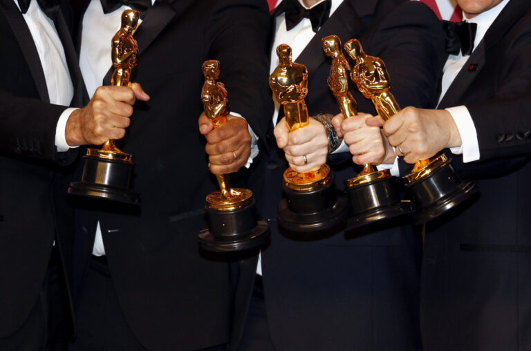 Osoby w garniturach trzymające statuetki Oscarów.