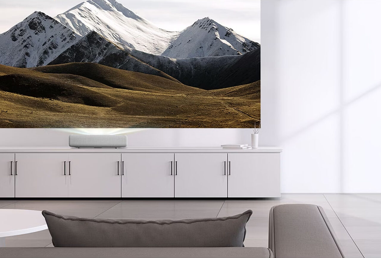Projektor Samsung LSP7T The Premier rzucający obraz pokazujący krajobraz górski na ścianę nowocześnie urządzonego salonu w jasnych kolorach.