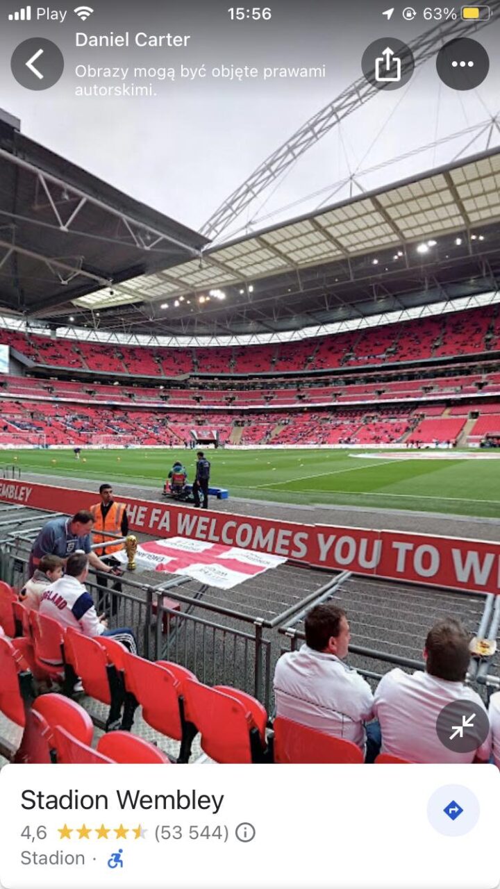 Widok wewnątrz stadionu Wembley z czerwonymi krzesełkami, z widzami na trybunach i napisem "THE FA WELCOMES YOU TO WEMBLEY" w przedniej części obrazu.