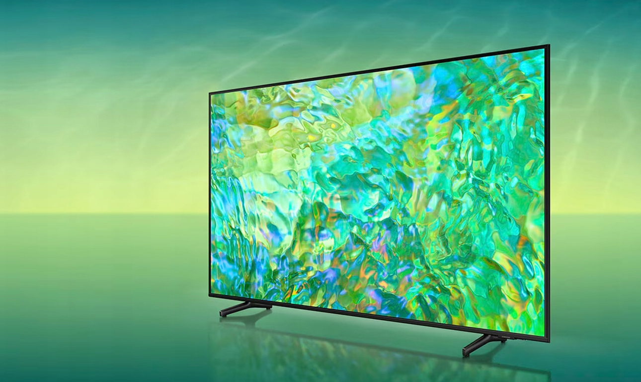 Telewizor z płaskim ekranem wyświetlający abstrakcyjny obraz z intensywnymi kolorami, imitujący rozmyte światła, ustawiony na stopkach z rozmytym tłem w odcieniach żółci i zieleni.