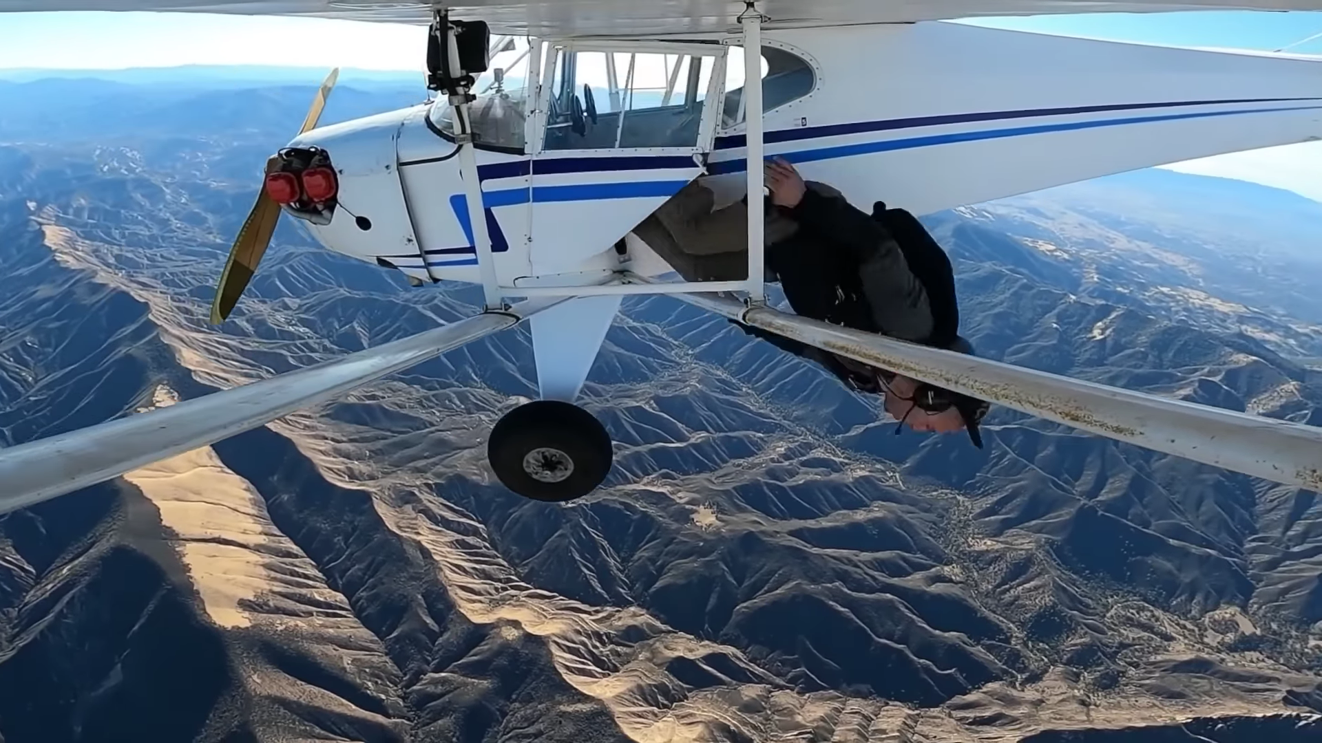 Widok na lecący samolot, Trevor Jacob wyskakujący ze spadochronem, w tle góry