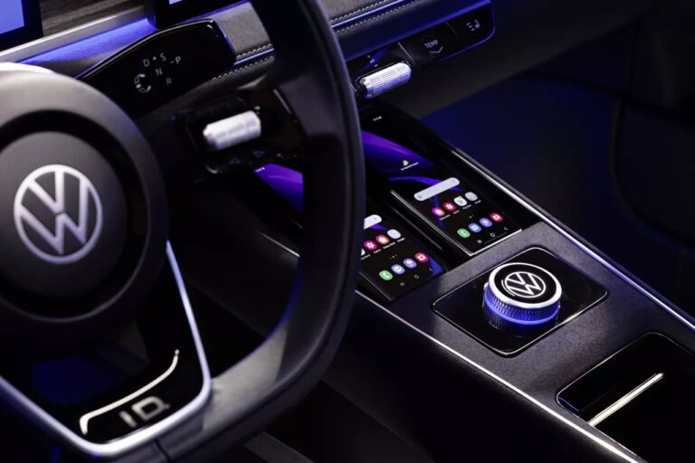 Wnętrze samochodu marki Volkswagen, widok na kierownicę z logo producenta oraz nowoczesną konsolę środkową z ekranami dotykowymi i pokrętłem Drive Mode.