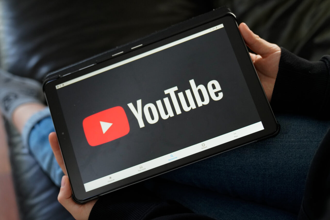 Tablet trzymany w rękach z wyświetlonym logo YouTube na ekranie.