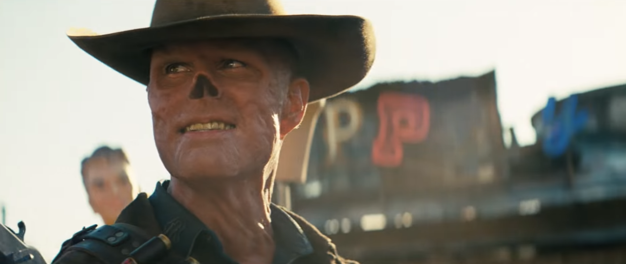 Mężczyzna w kowbojskim kapeluszu patrzy w dal na tle rozmazanych liter "P" i "P" oraz konturów budynków.