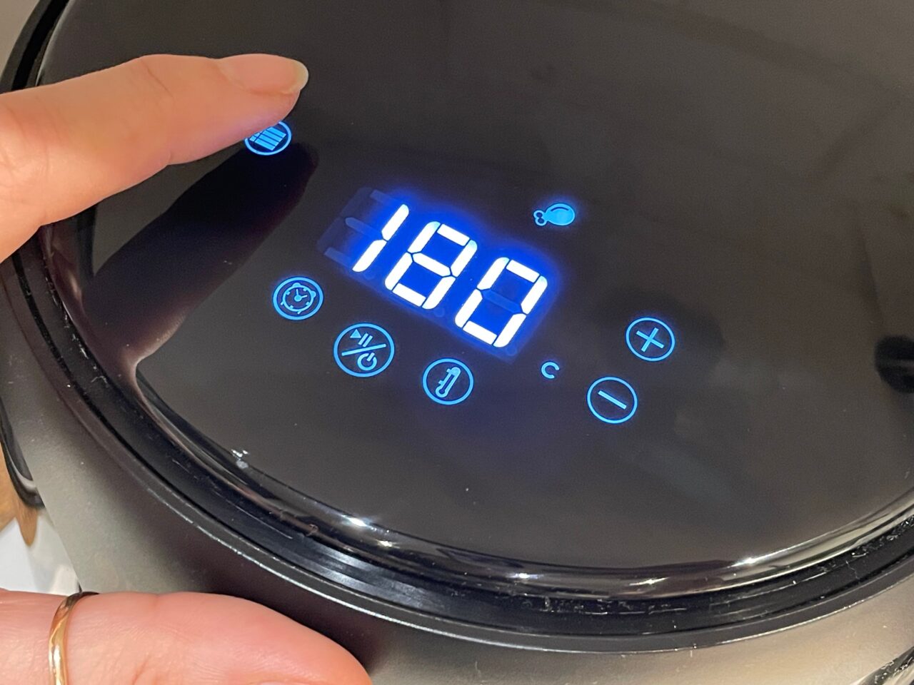 Panel sterowania czarnego urządzenia kuchennego z niebieskim podświetleniem pokazujący temperaturę 190 stopni Celsjusza, z dłonią dotykającą ekranu.