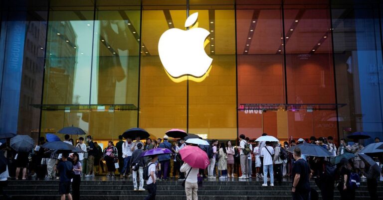 Tłum ludzi z parasolami przed sklepem Apple z dużym logo firmy podświetlonym na żółto.