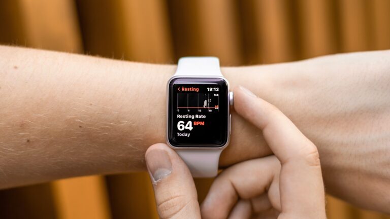 Osoba dotyka ekranu smartwatcha, który wyświetla pomiar tętna spoczynkowego równego 64 uderzenia na minutę.