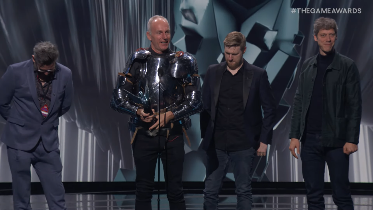 Czterech mężczyzn na scenie podczas ceremonii wręczenia nagród The Game Awards za Baldur's Gate 3; drugi od lewej ma na sobie lśniący, srebrny kostium przypominający zbroję.