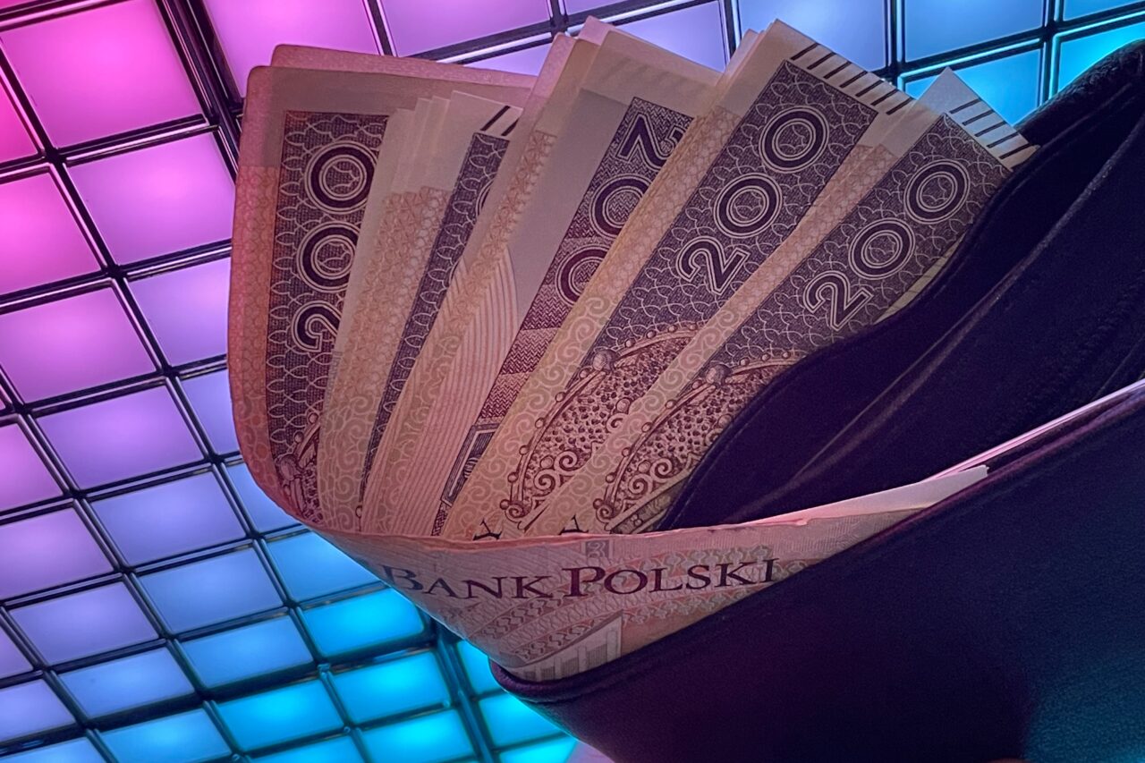 Banknoty o nominale 200 zł zwrot podatku ułożone wachlarzowo na ciemnym tle z rozświetlonym, kolorowym sufitem w tle.